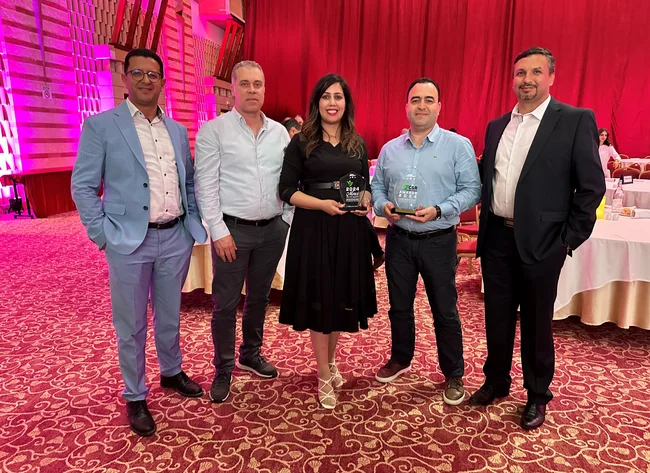 Five people smile at the camera. Two of them are holding the CSR Award.