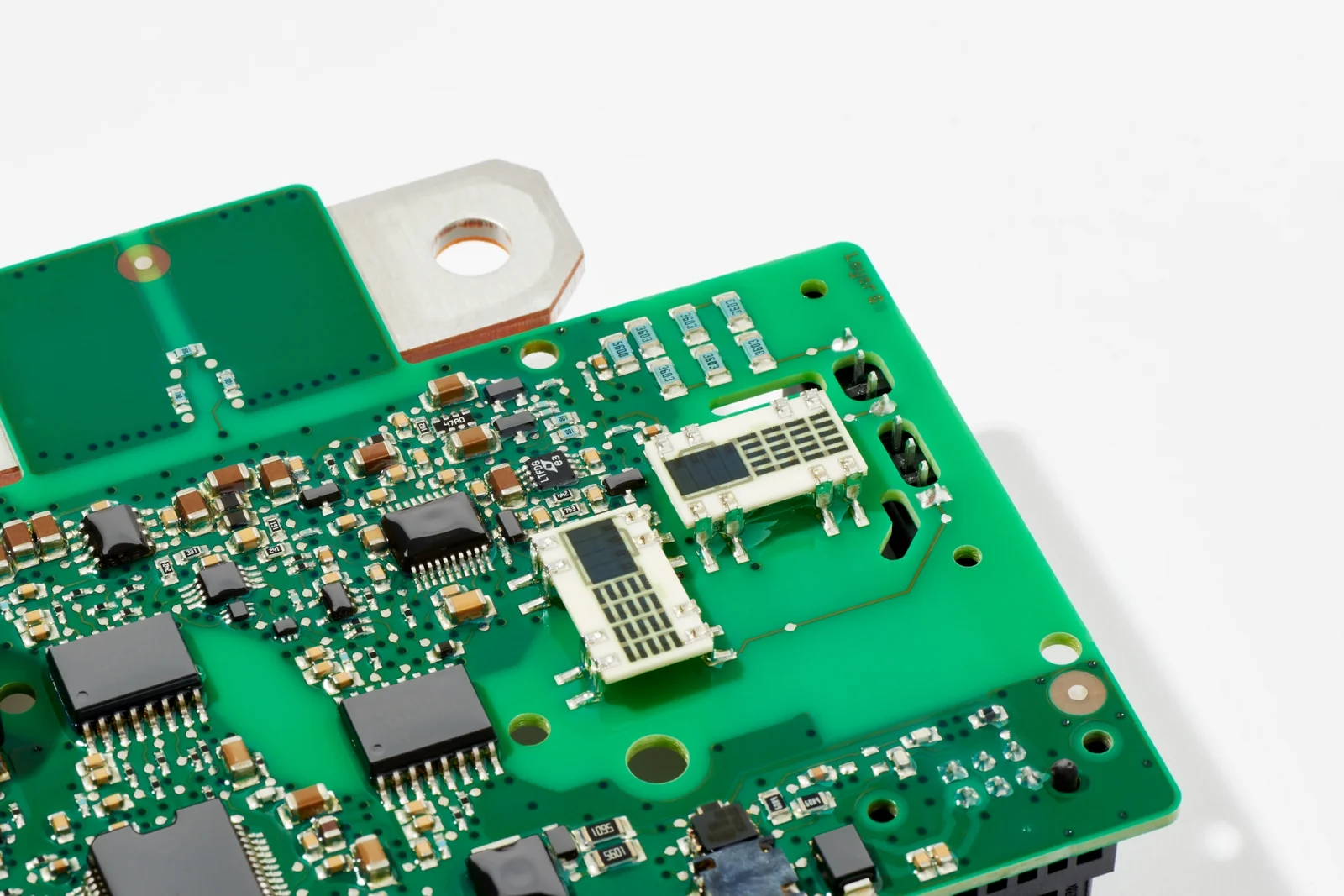 A section of a rectangular dark green circuit board lying on a white surface.