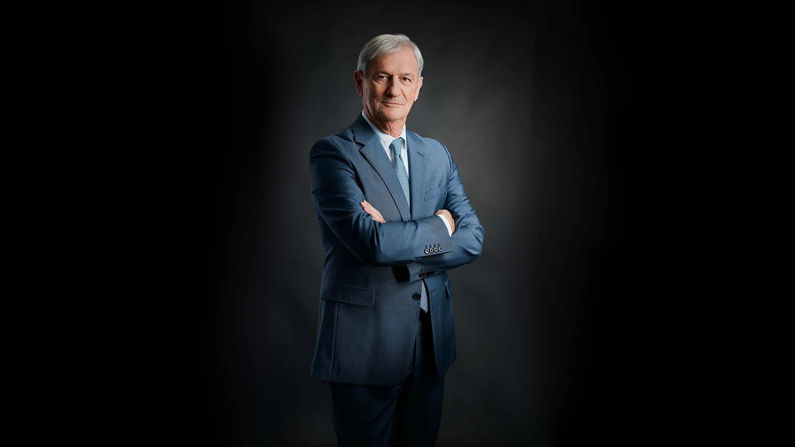Fritz Dräxlmaier stands smiling with his arms crossed in front of a black background.