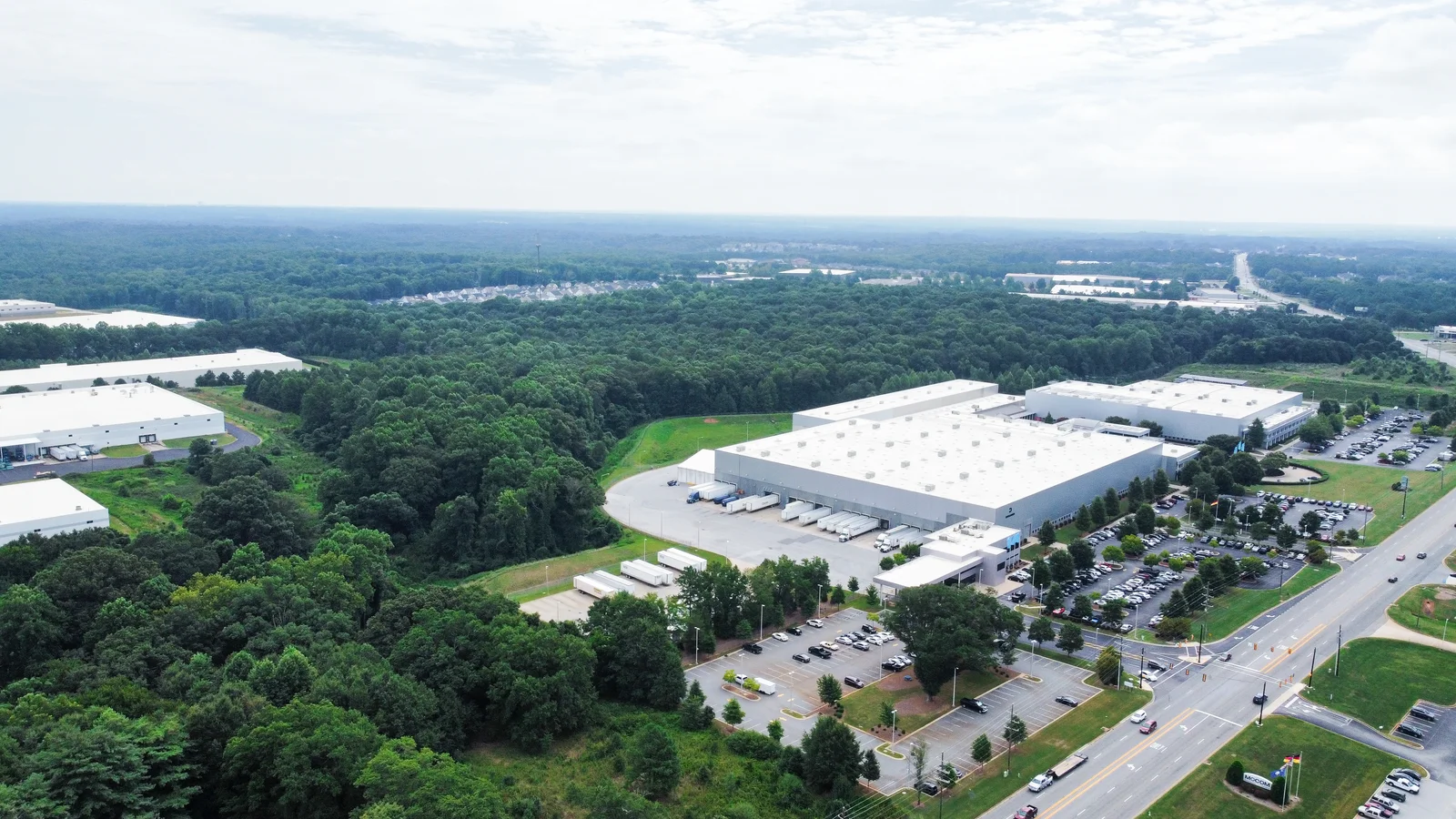 Luftaufnahme eines großen DRÄXLMAIER-Industriegebäudes in Duncan mit Parkplatz, umgeben von Wald und Straßen.